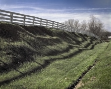 The white fences and blue grass give this horse farm a distinctive look as the shadow undulates along the embankment.  Lexington KY.