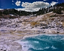 The turquoise-colored water combined with the impossibly colored volcanic ash on the shore is bracketed by more normal looking trees and sky.  Lassen Volcanic National Park, Mineral, CA.