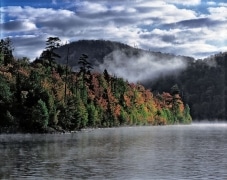 Vibrant fall colors on Lake Superior as low clouds drift between the hills and fog hovers over the water.  A very special moment.  Lake Superior Provincial Park, Canada.