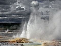 Clepsydra Geyser spouts off on the Fountain Paint Pot Trail as storm clouds gather behind.  Yellowstone National Park, WY.