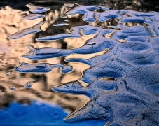 Light bouncing off the canyon walls is reflected in water surrounding the muddy silt which in turn reflects the clear blue sky.  Slot canyon in Zion National Park, UT.