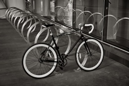 A lone bicycle parked in a bike stand gives the impression of many more bikes behind it due to the reflection of the stands in the window.  Transbay transit center, San Francisco.